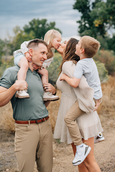 parents kissing while holding their son and daughter on dad's shoulders