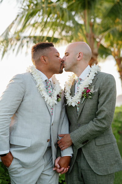 A newlywed couple in suits holding hands and kissing 