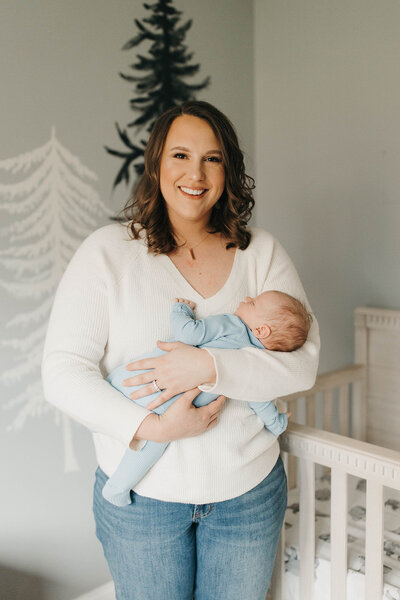 Brunette woman holding her newborn son while smiling at camera