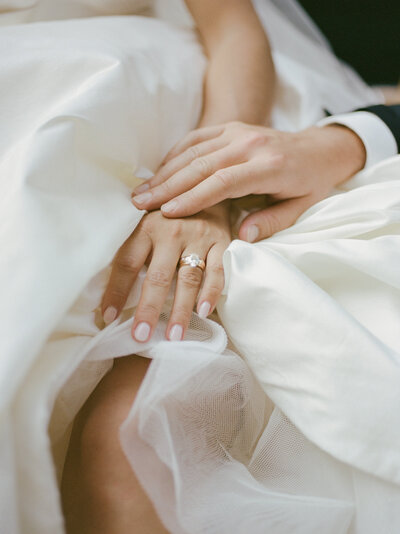 a groom's hand rests lovingly on his bride's, showing her diamond engagement ring & wedding band in Detroit, Michigan