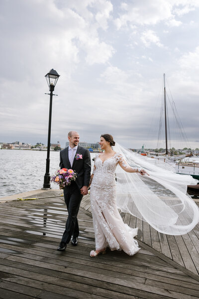 bride and groom walking with her veil blowing in the wind near sagamore pendry and frederick douglass maritime park wedding venues