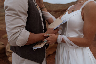 Couple holding their vows books with their wedding dress and suit on while also embracing 