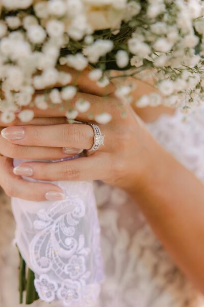 Bride details of ring holding bouquet of baby's breath flowers.