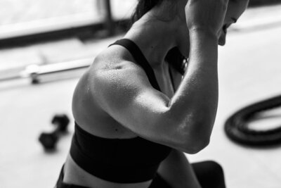 Close-up of a woman’s muscular arm and shoulder during an intense workout, showing strength and sweat in a gym setting.