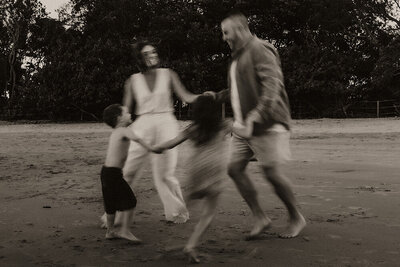 Blurry candid photo of a joyful family playing together barefoot on the beach in black and white
