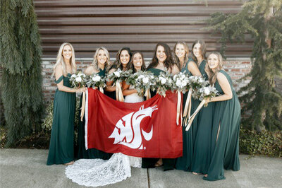 Bride poses with bridesmaids holding their college alma mater flag