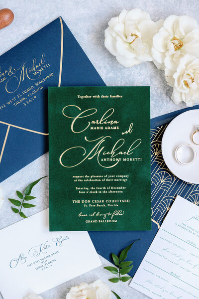 Wedding invitation ideas featuring a gold foil wedding invitation on forest green velvet, a foil-stamped envelope liner on royal blue, and a gold-trimmed royal blue envelope.