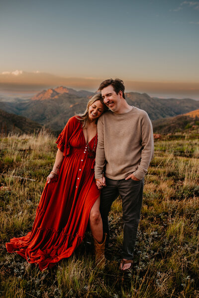 A beautiful woman in a flowy dress holds hands and laughs with her husband in the Rocky Mountains