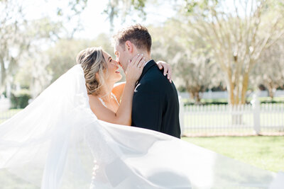 bride and groom kissing while wrapped in veil