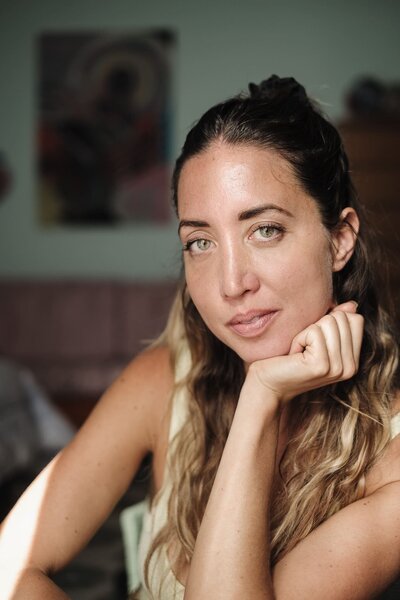 Close-up portrait of a woman, her chin resting in her hand as she looks directly at the camera