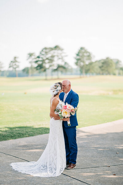 Woman in white dress hugging man in blue suit standing on concrete outside