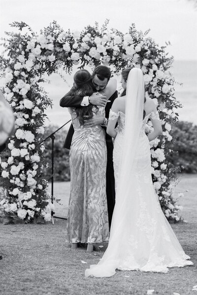 A person hugging a wedding participant as their partner looks on 