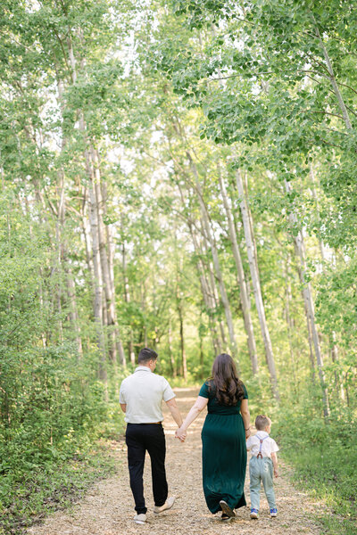 a family holds hands as they stroll down a nature path, surrounded by green aspen trees