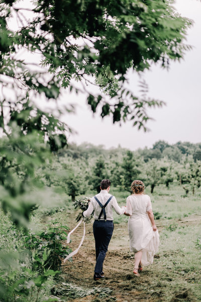 bruidspaar loopt in boomgaard met bruidsboeket