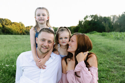 family of 4 mom, dad, and 2 daughters smiling at camera. mom with cherry red hair smiling at girls