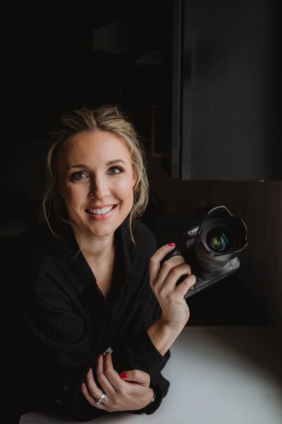 Headshot of lead photographer with camera in hand smiling at camera