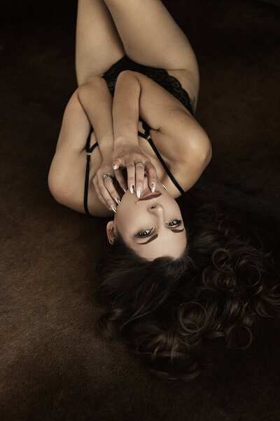 Woman with curly hair in a black bodysuit, posing with confidence in a dimly lit room