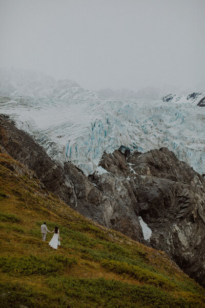 Couple walks to the edge of a cliff overlooking a giant glacier