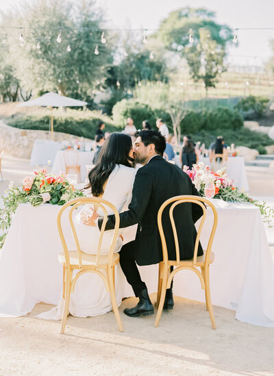 bride and groom kiss at sweetheart table at garden venue
