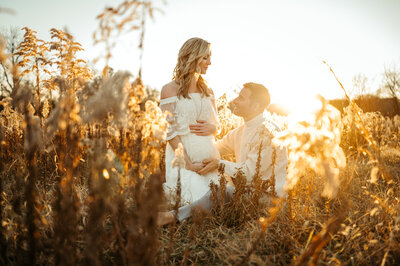 Pregnant couple snuggled up in a glowing PA field at sunset. 