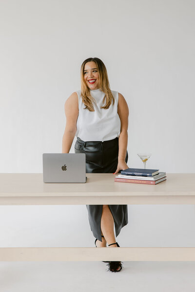 Natasha Churches, owner of Aisle & Co., poses for a headshot in all white while holding champagne.