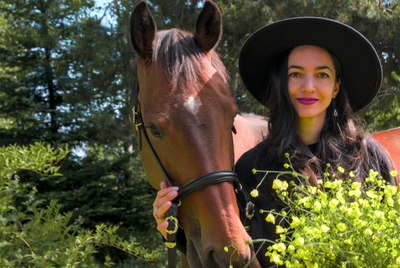 Animal Communicator standing beside her bay horse holding a bouquet of yellow flowers. 