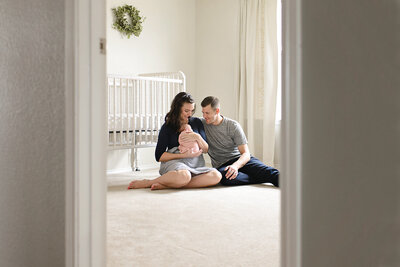 New parents sitting in front of a white crib in the nursery during a baby photo shoot.
