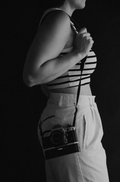 side profile body photo in light and shadow of a women holding a camera on her shoulder.