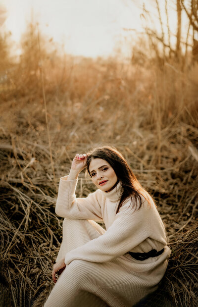 a young woman wearing turtleneck beige dress sitting on a ground