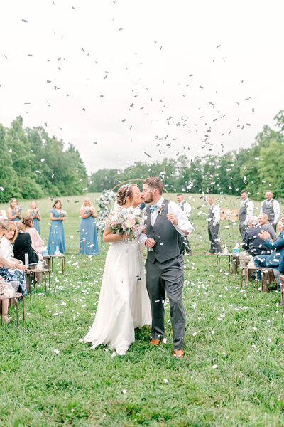 Bride and Groom share a kiss as they walk down a confetti filled aisle
