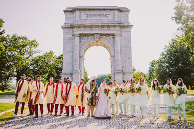 sikh bride and groom walking with their bridal party in front of the arch at valley forge national historical park in pennsylvania