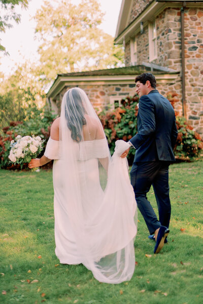 A couple walks away in front of a stone building on their wedding day.