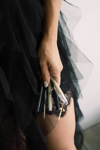 Cat Lauren Calligraphy in black tulle dress holding calligraphy pens