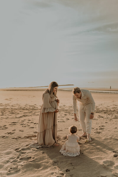 Gezin speelt op het strand tijdens zwangerschapsshoot / gezinsshoot