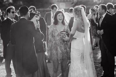 Natural light black and white wedding photo of the bride chatting to her guests at Goodwood House with sun flare, taken in a true documentary style by Adorlee