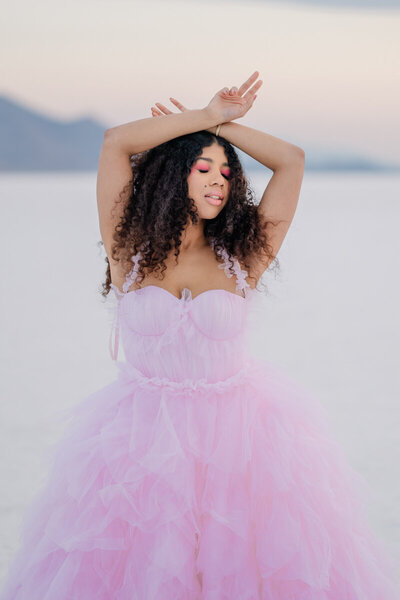 woman in pink tulle dress holding her hands above her head with her eyes closed