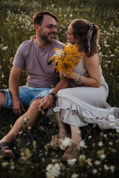 Pärchen sitzt auf einer Blumenwiese und lachen sich an