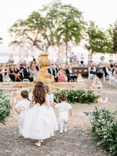 Bride smiling over her shoulder while holding a lush pink and white bouquet in the stone streets of Altos de Chavón — captured by Asia Pimentel Photography.