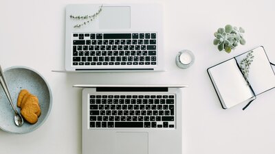 birds eye view of two open laptops standing back, with a candle, notebook, and plant next to them