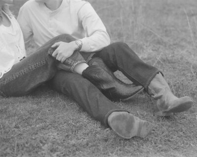 Black and white image of a couples' legs resting on each other while both are wearing jeans and boots