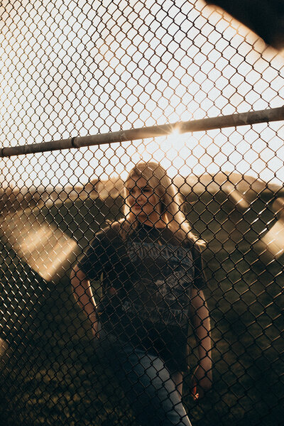 Creative brand portrait taken by Sunshine Coast photographer, capturing golden sunlight and raw personality behind a chain-link fence.