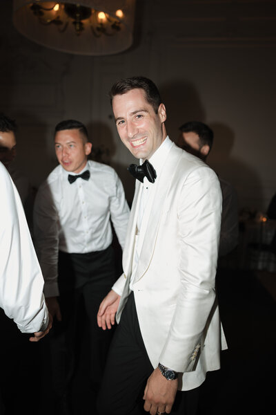 Candid direct flash photo of groom dancing in a luxury off-white tuxedo during a Philadelphia wedding reception.