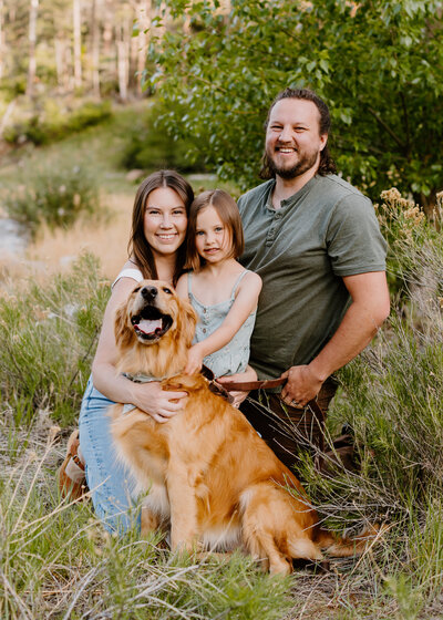 Family portrait with parents, daughter, and golden retriever in a natural setting, captured by a Colorado Wedding and Portrait Photographer.