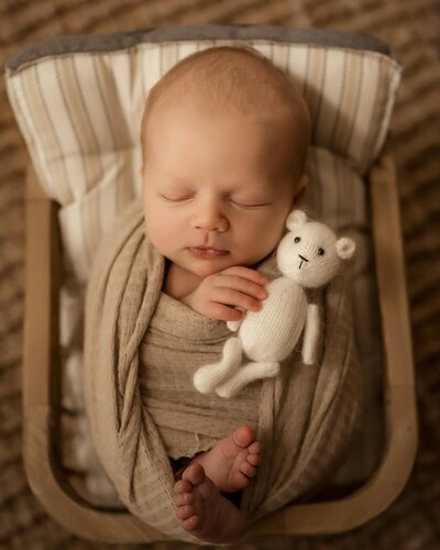 The enchanting world of newborn photography with our investment page, featuring a serene image of a baby boy peacefully sleeping in a brown basket. Dressed in a tiny white outfit, the newborn exudes pure innocence and charm.