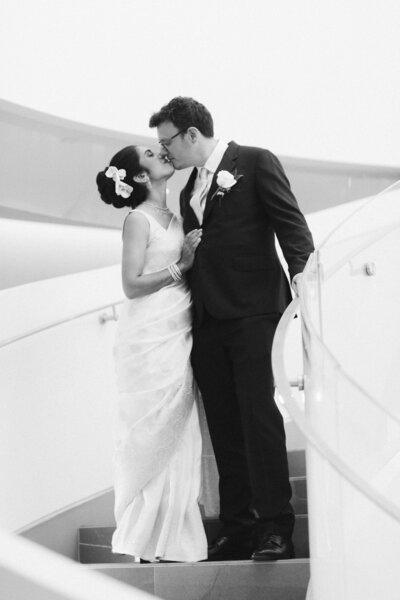 Elegant wedding portrait of bride and groom sharing a kiss on modern curved staircase at The Pearl Hotel in Burlington, Ontario.