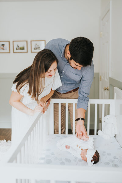 New parents in nursery look into crib with sleeping newborn baby girl during photo session with Worth Capturing Photography
