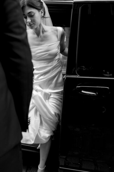 Bride exiting ceremony car in her wedding gown, ready for the aisle.
