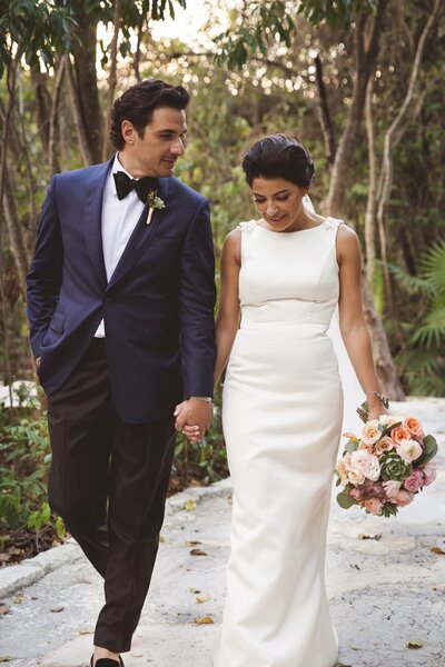 Groom looking at bride as they walk down path after wedding in Riviera Maya