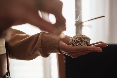 Close-up of hands holding a Desert Rose crystal with incense burning above it, during an energy healing session.