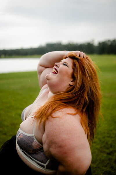 woman smiling as she poses outside for her boudoir photos in a purple bra
